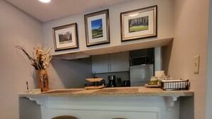 Una cucina con angolo bar, due sgabelli, quadri appesi e un vaso con piante essiccate.