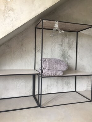 Une pièce dotée d’un plafond et de murs en béton, avec une structure de lit superposé en métal et un luminaire suspendu.