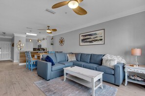 A modern living room with a blue sectional sofa, a white coffee table, and a dining area with blue chairs.
