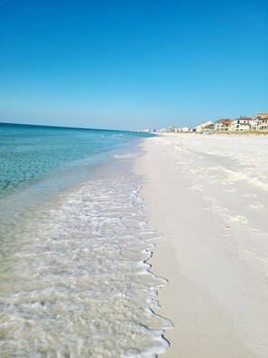 Ein Strand mit klarem Wasser, Sandstrand und Gebäuden im Hintergrund.