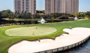 A golf course with bunkers, a pond, and a bridge.