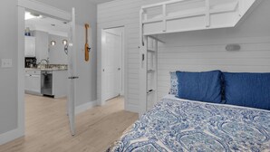 Ein Schlafzimmer mit Etagenbett, ein Badezimmer mit Waschbecken und ein durch eine offene Tür erreichbarer Küchenbereich.