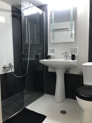 Een moderne badkamer met een glazen douchecabine, een wit wastafeltje en een toilet.