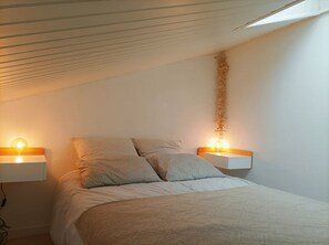 Quarto com uma cama, duas mesas de cabeceira e um candeeiro fixado na parede.