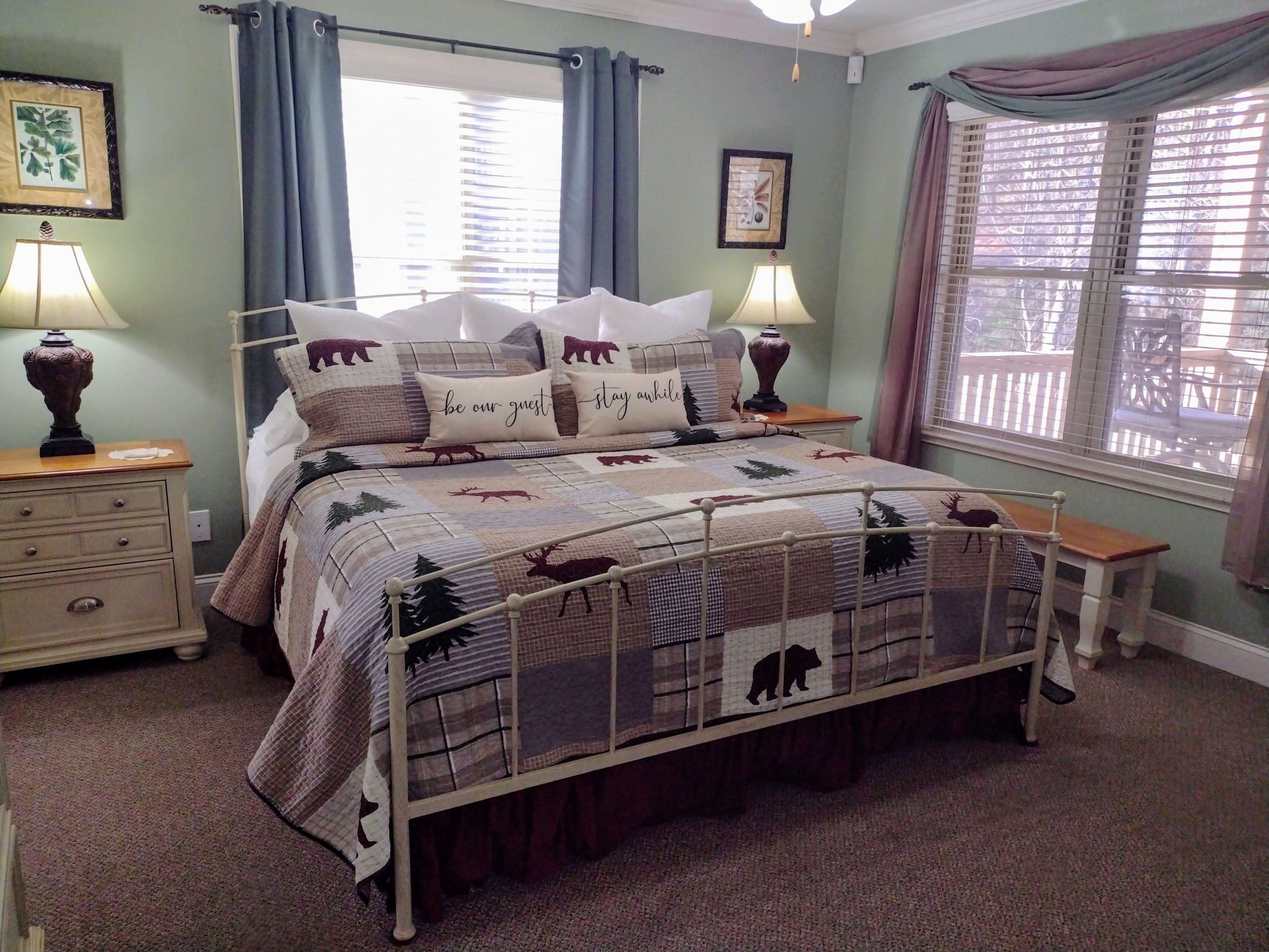 A bedroom with a bed, two bedside tables, a window with curtains, and a wall with two framed pictures.