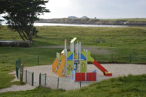 Ein Spielplatz mit Rutschen und Klettergerüsten, umgeben von einem eingezäunten Bereich mit Sandboden.