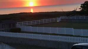 Un atardecer sobre una zona costera con una valla blanca y un edificio al frente.