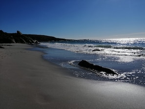 A beach with a curved shoreline, rocky outcrops, and waves approaching the shore.