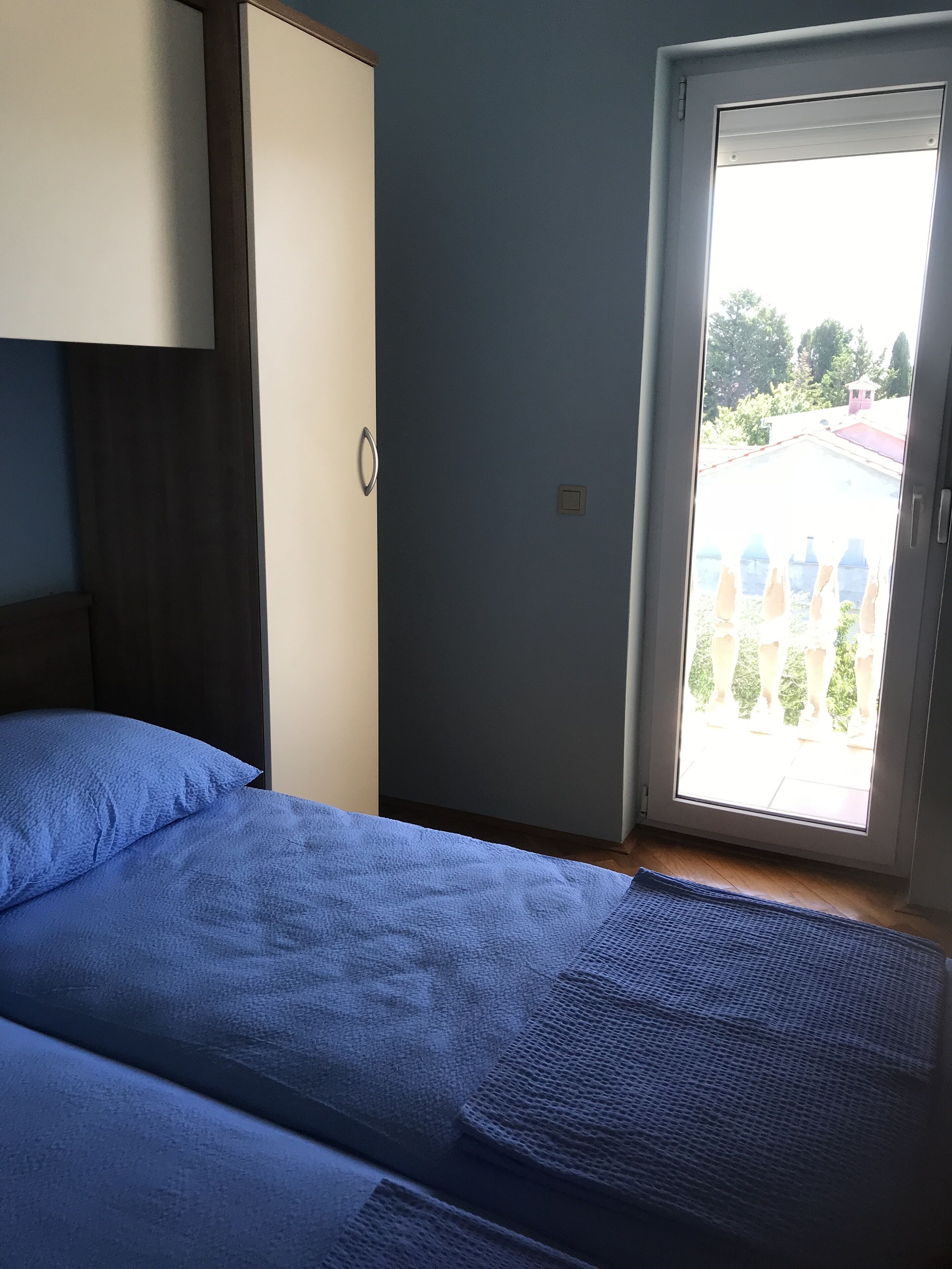 A bedroom with two beds, a wardrobe, and a sliding glass door leading to an outdoor area.