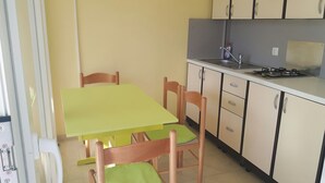 Een kleine keuken met een tafel, stoelen, een spoelbak en keukenkastjes.