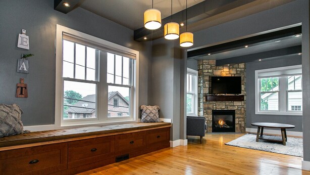 A spacious living room with a built-in bench, large windows, a stone fireplace, and a flat-screen TV. - Modern home in historic neighborhood with lower level game room by Loras College (Dubuque)