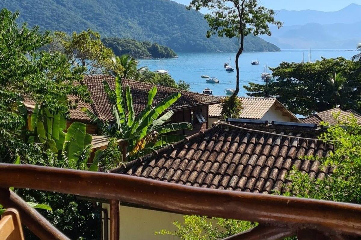 A terrace with a view of a coastal landscape, including boats on the water and a mountainous backdrop.