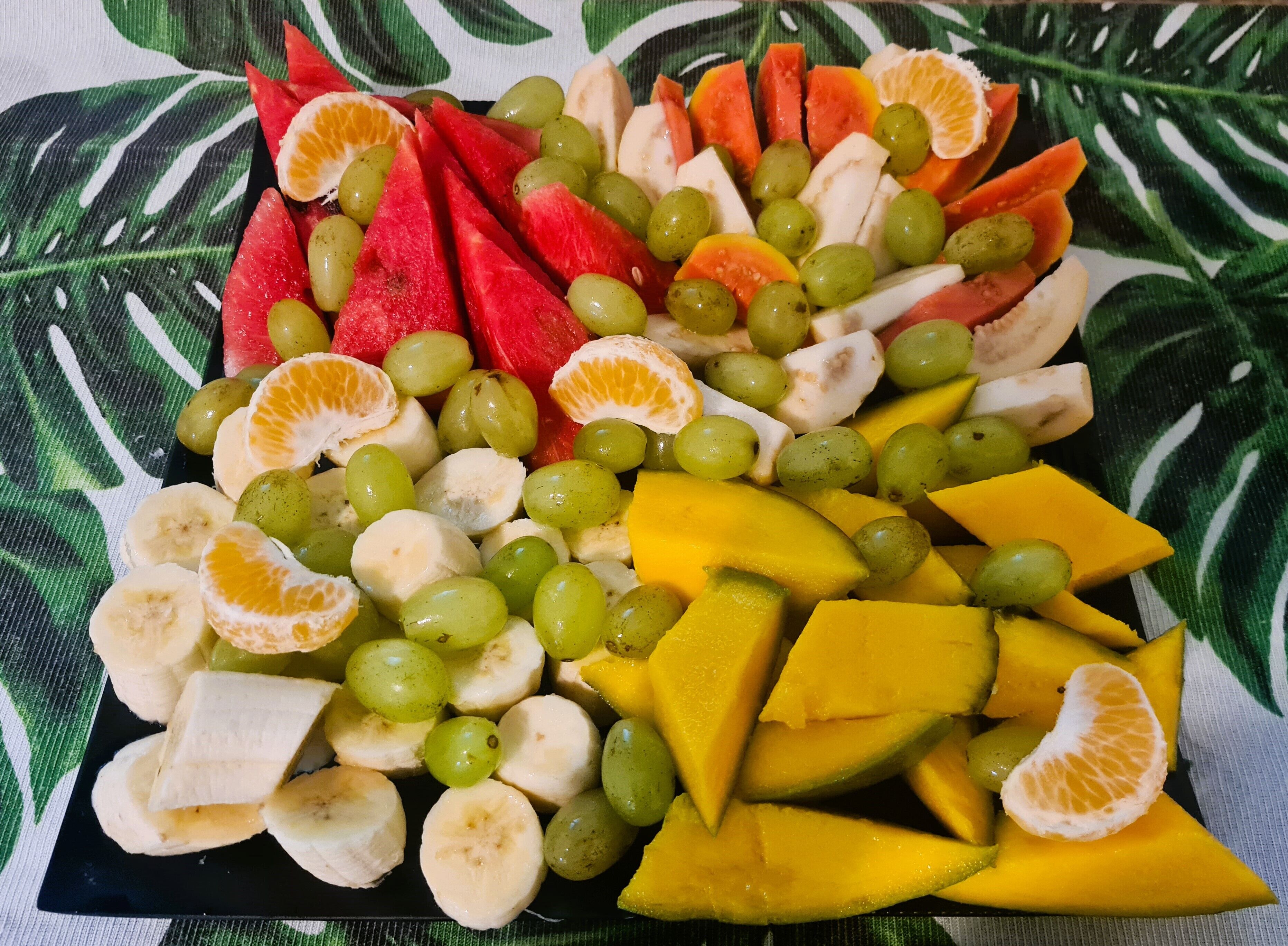 A fruit platter with various fruits including bananas, grapes, watermelon, and mango slices.