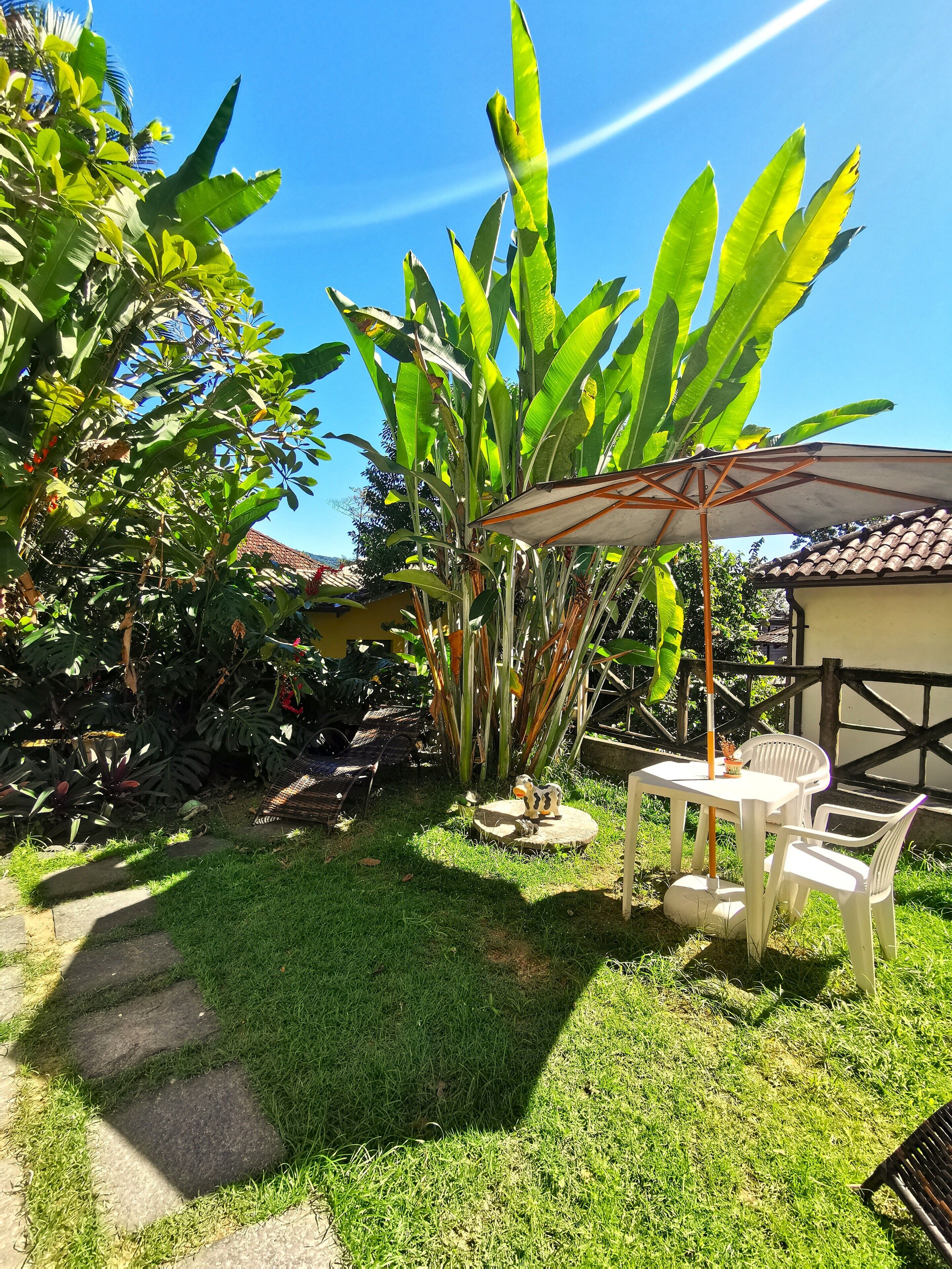 A patio area with a table and chairs, surrounded by lush greenery and a large umbrella.