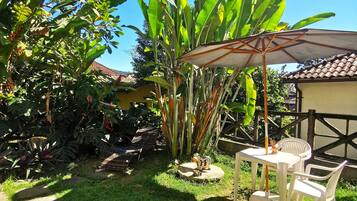 A patio area with a table and chairs, surrounded by lush greenery and a large umbrella.