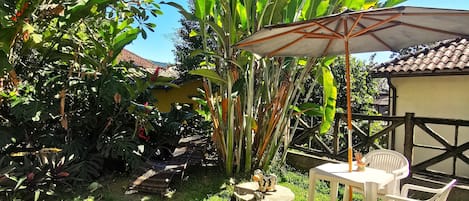 A patio area with a table and chairs, surrounded by lush greenery and a large umbrella.