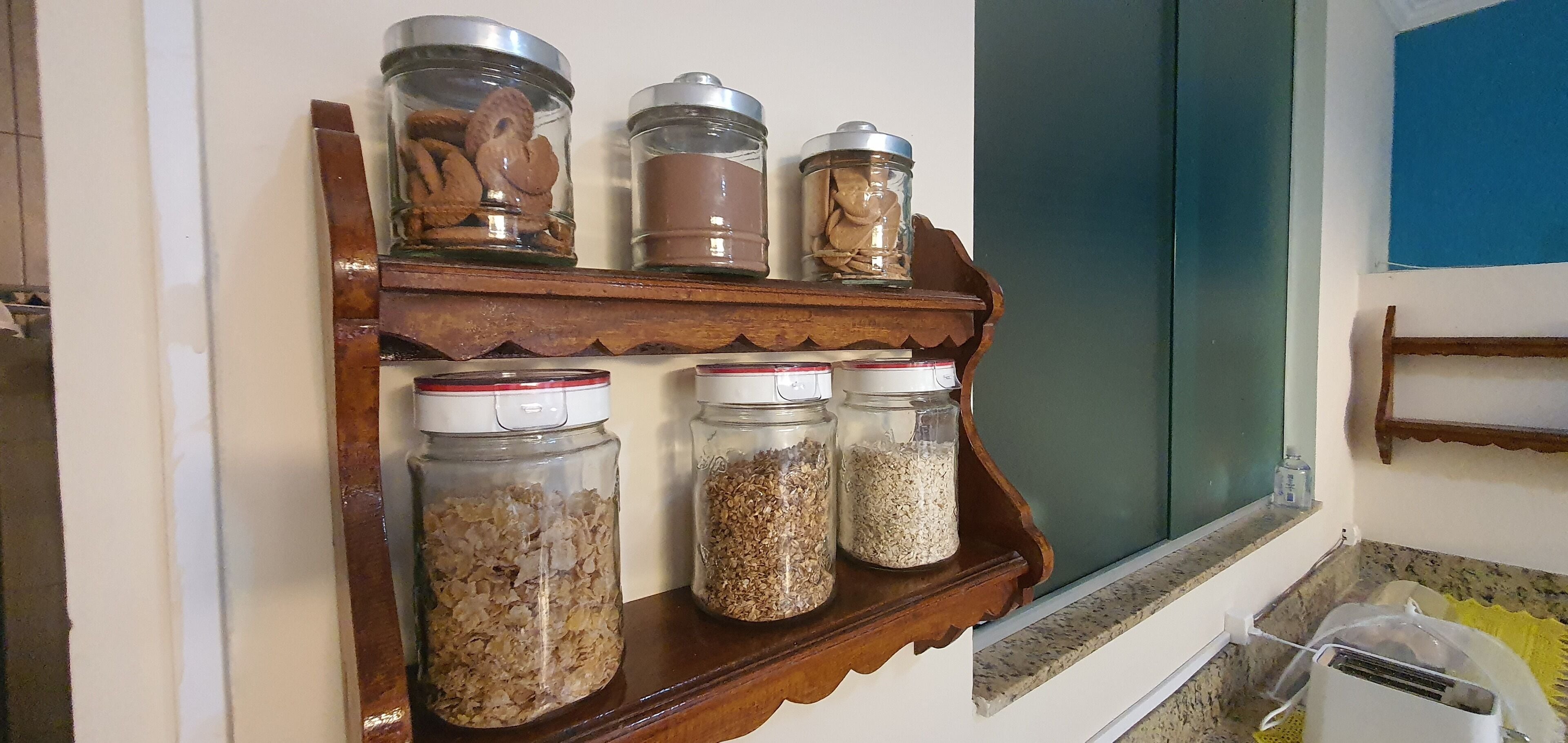 A kitchen shelf with jars containing cookies, chocolate, and grains.