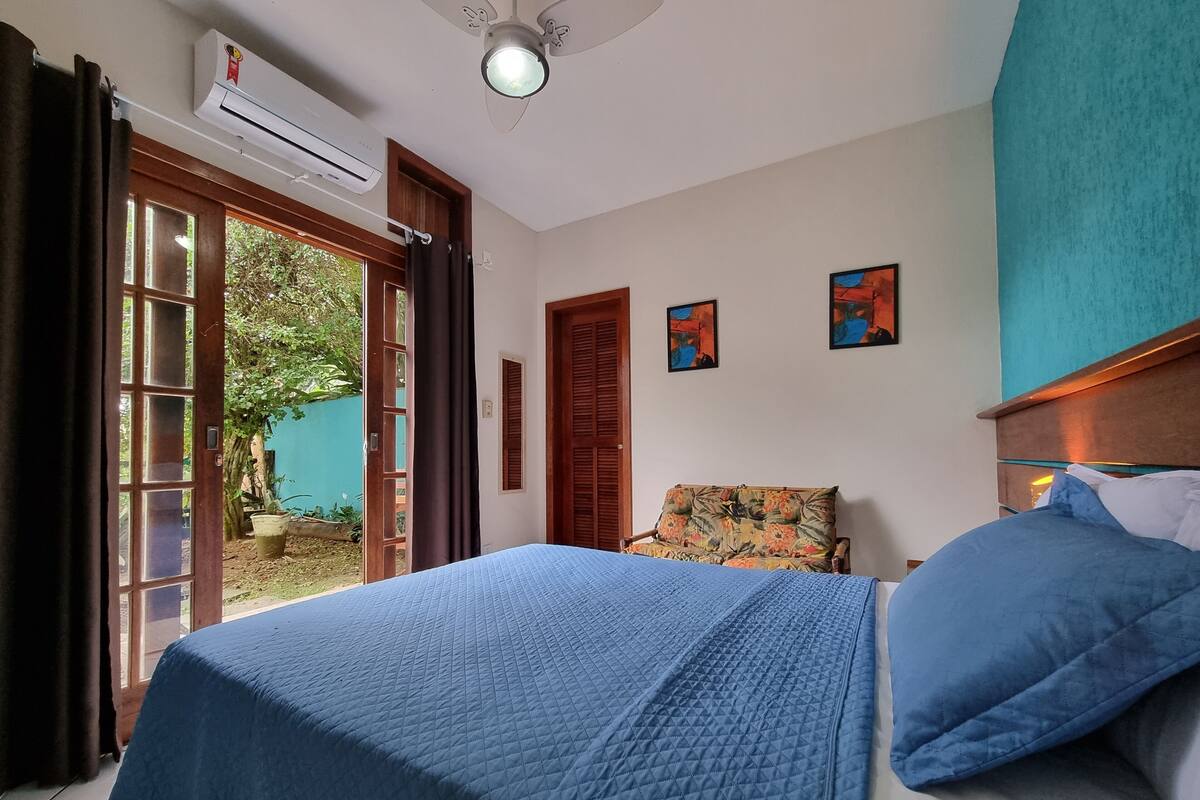 A bedroom with a bed, a chair, an air conditioning unit, and a door leading to an outdoor area.