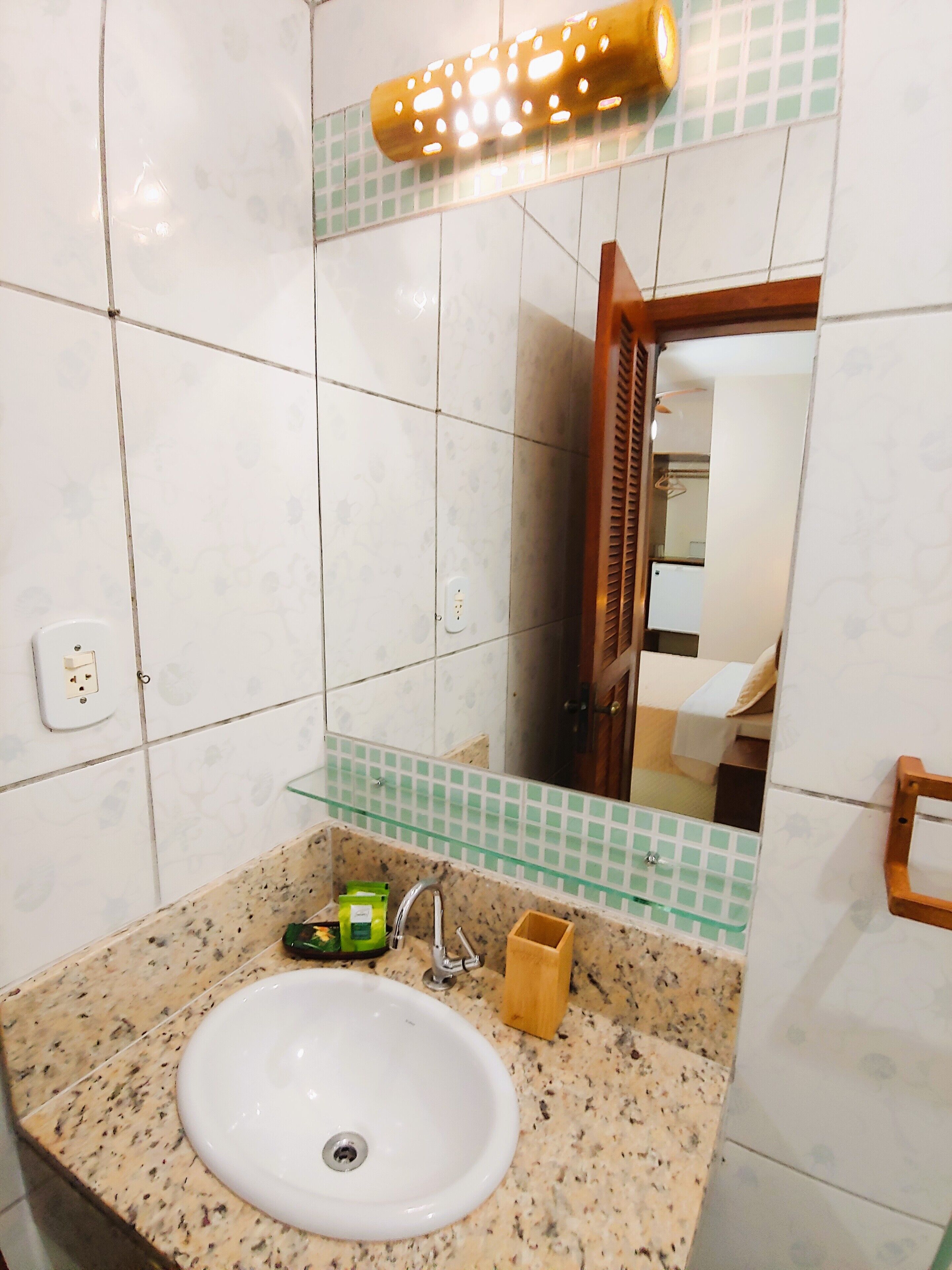 Un baño con encimera de granito, un lavamanos blanco, un espejo y un estante de vidrio verde.