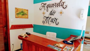 A reception desk with a wooden finish, a hanging pendant light, a wall with a teal and white color scheme, and a sign that reads "A guarda do Mar". - Pousada Aquarela do Mar (Angra dos Reis)
