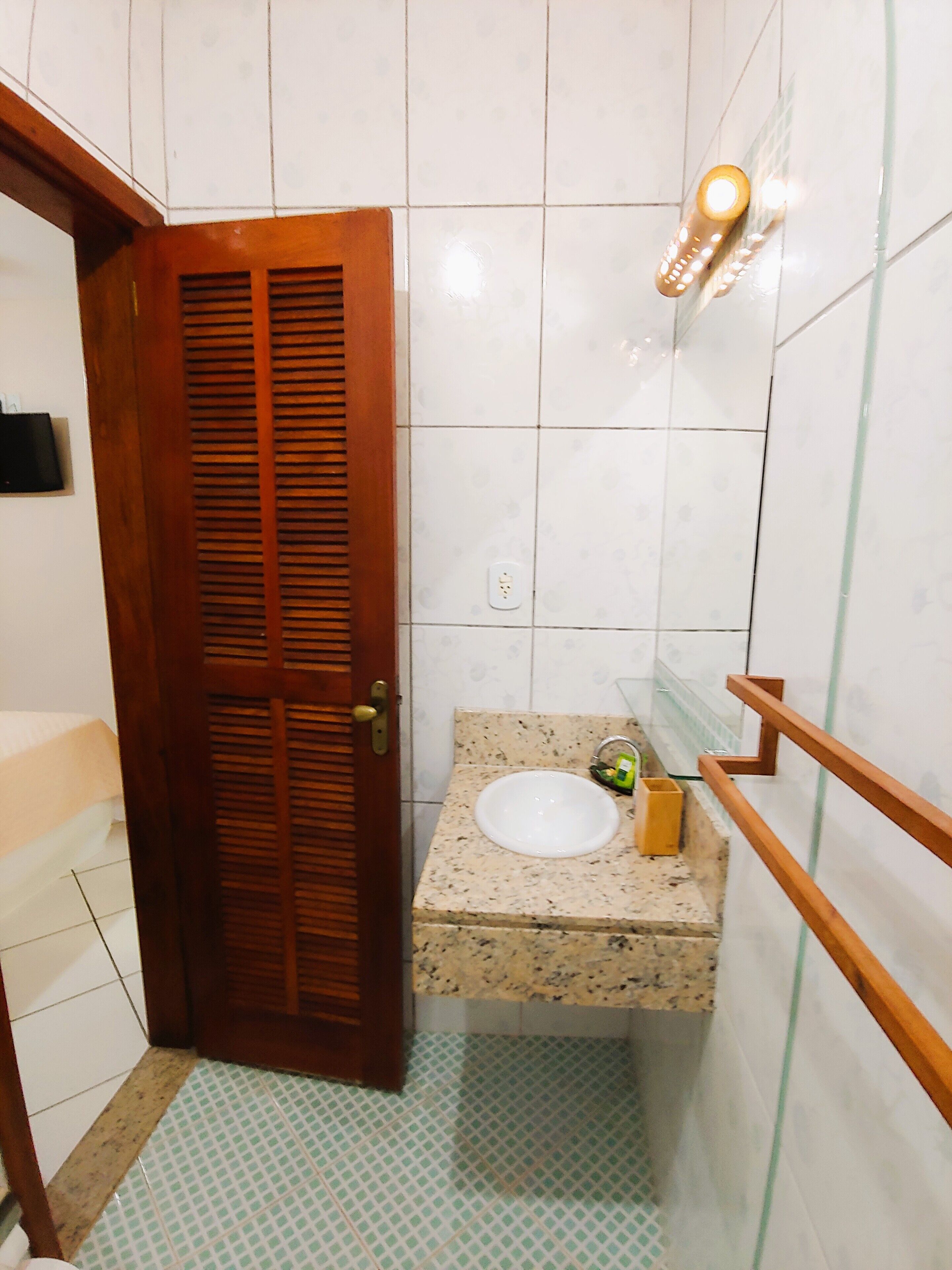 A bathroom with a wooden door, a sink with a marble countertop, and a mirror with a light fixture.