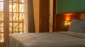 A bedroom with a bed, a nightstand, a lamp, and a view of the outside through a window with shutters. - Pousada Aquarela do Mar (Angra dos Reis)