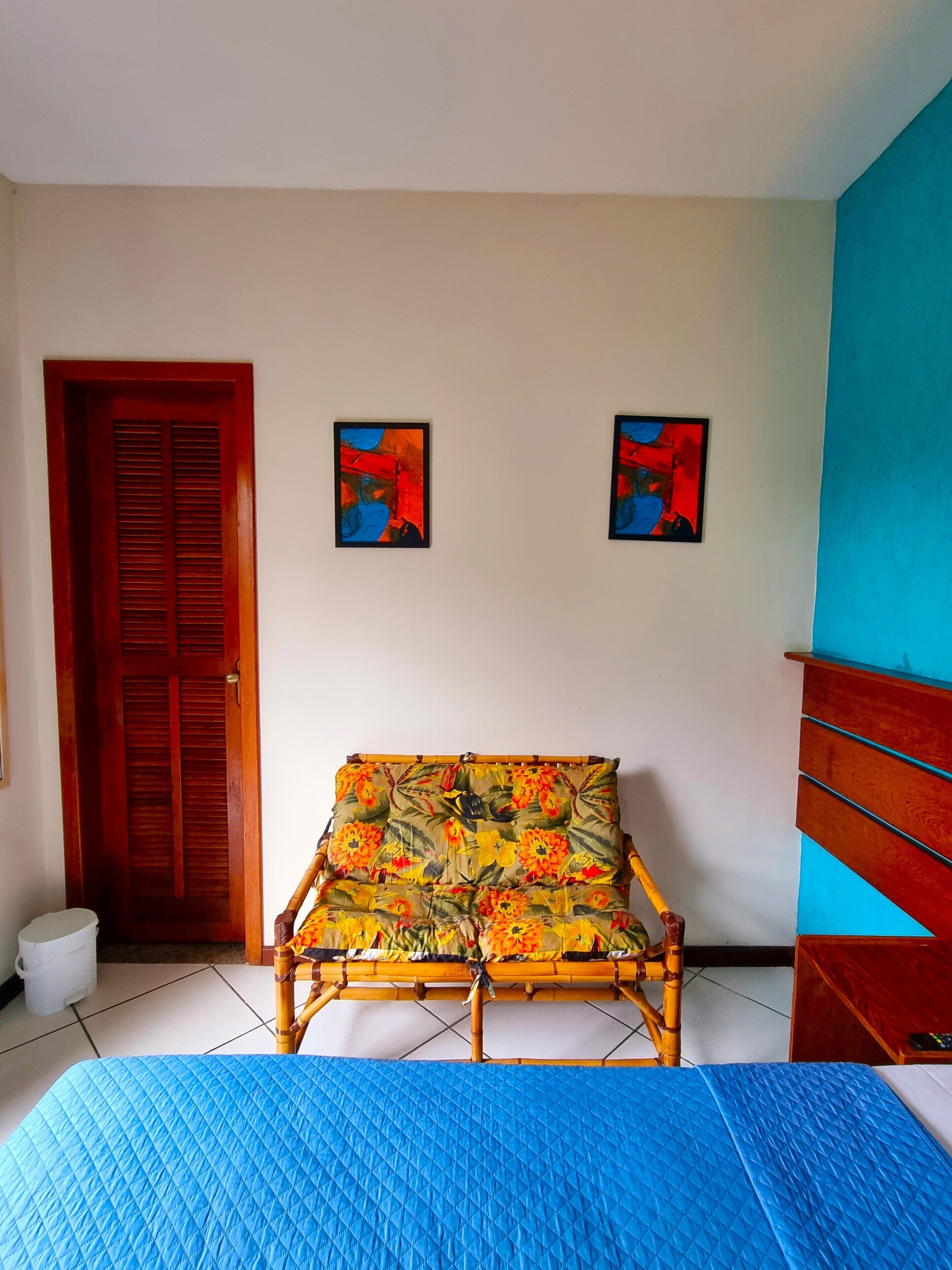 A room with a bed, a wooden door, and two abstract paintings on the wall.