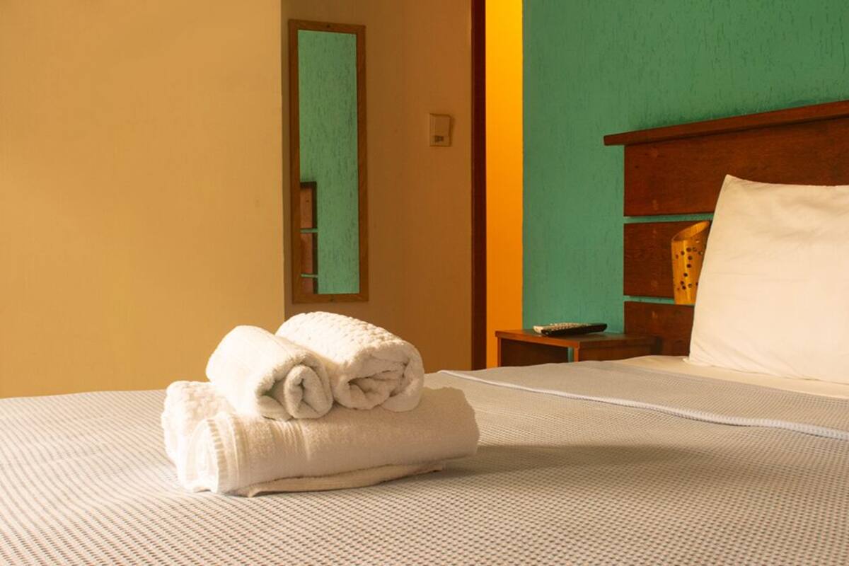 A neatly made bed with a folded towel, a wooden headboard, and a nightstand with a lamp.