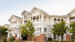 A multi-story residential building with a symmetrical facade, multiple balconies, and a brick foundation. - One Bedroom, Luxury Condo, Williamsburg Parkside, Virginia (2629717) (Williamsburg)