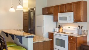 A compact kitchen with wooden cabinets, a white refrigerator, a microwave, a stove, and a granite countertop. - One Bedroom, Luxury Condo, Williamsburg Parkside, Virginia (2629717) (Williamsburg)
