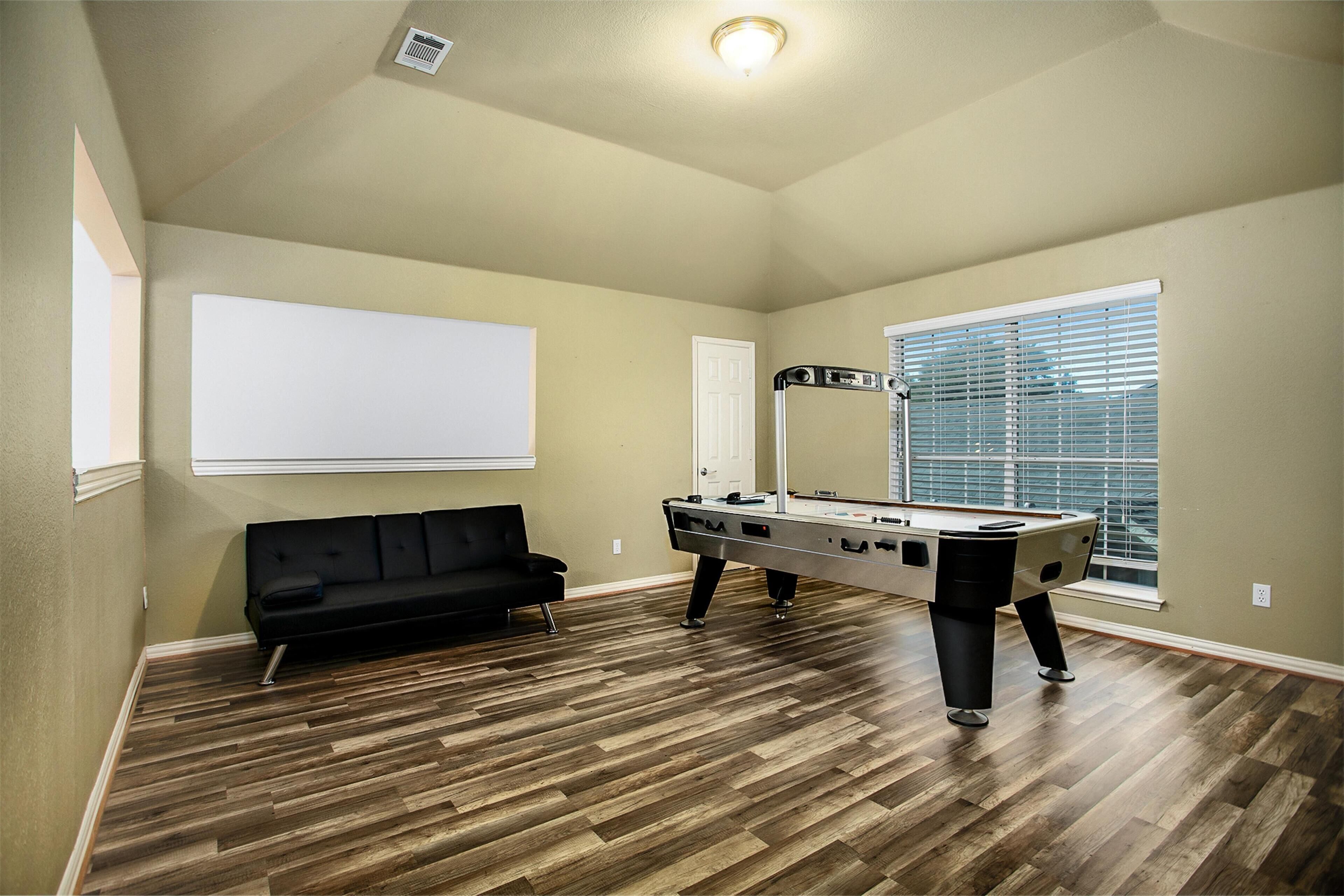 A room with a pool table, a black sofa, and a large window with blinds.