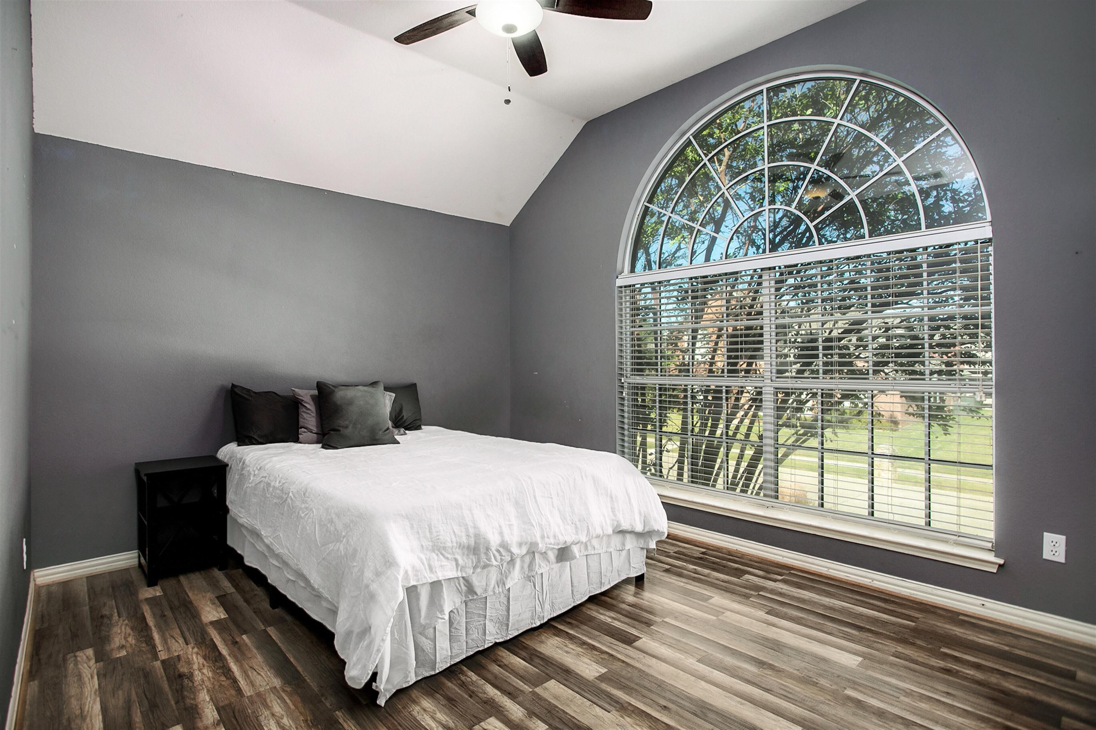 A bedroom with a large arched window, a bed with white bedding, and a ceiling fan.