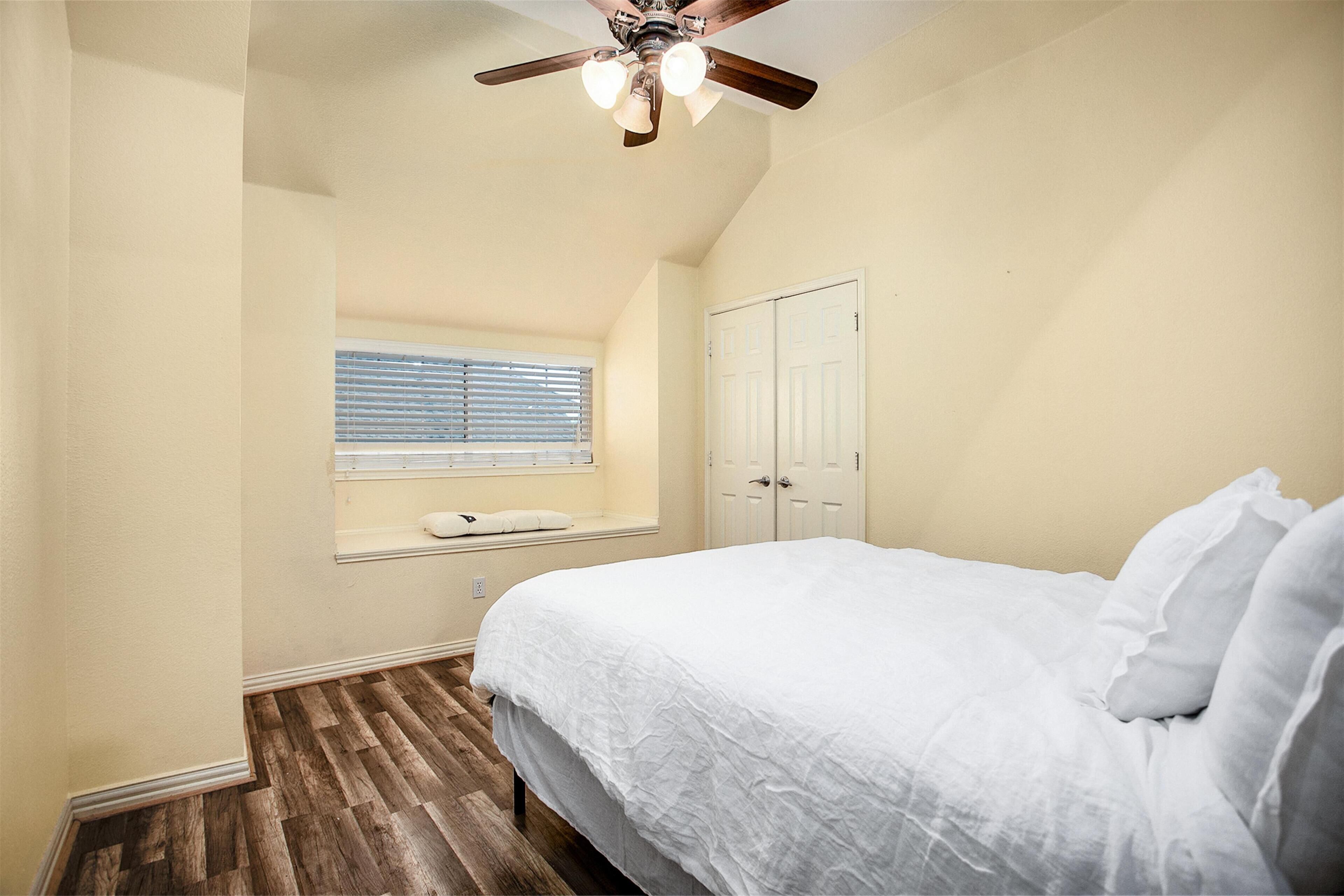 A bedroom with a bed, a ceiling fan, a window with blinds, and a door.