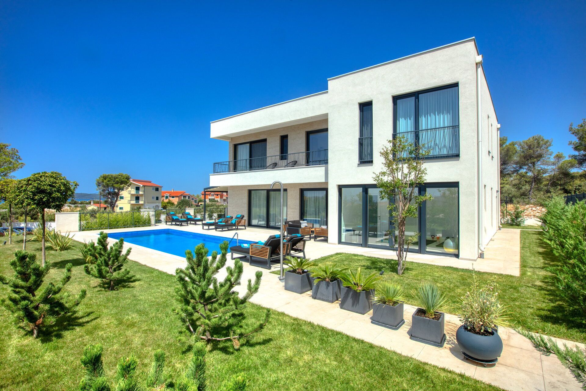 A modern two-story house with a swimming pool, outdoor seating, and a well-maintained garden.