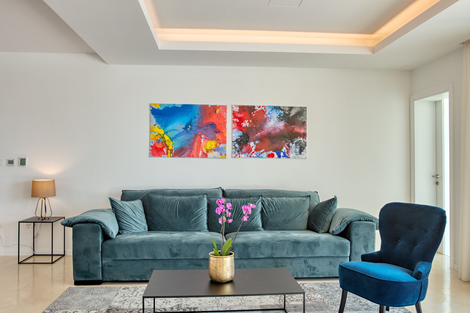 A modern living room with a teal sofa, a blue armchair, and a coffee table with a flower vase.
