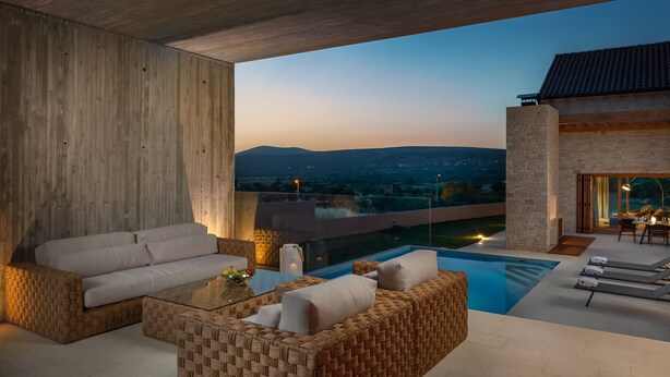 Un espacio exterior moderno con piscina, mobiliario de mimbre y vistas a colinas distantes.