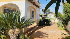Un patio con un sendero adoquinado, palmeras y un edificio con arcos y tejado de tejas.