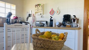 Una cocina con una silla blanca, una cesta de mimbre para fruta en una mesa y diversos electrodomésticos.