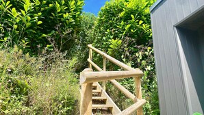 Una escalera de madera que sube a un edificio rodeado de abundante vegetación.