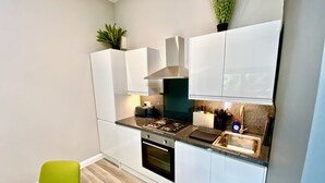 Una cocina moderna con armarios blancos, una estufa a gas y un horno empotrado. Hay dos sillas y una pequeña mesa.