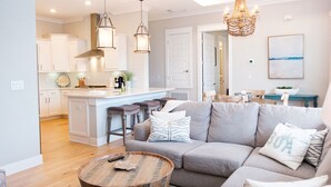 Ein modernes Wohnzimmer mit einem grauen Sofa, einem runden Couchtisch und einem Küchenbereich im Hintergrund.