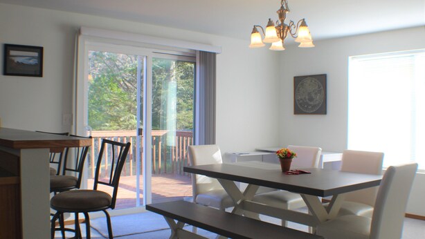 A dining area with a table, chairs, and a bench. There is a balcony with a view of trees. - Canal front Island Escape for the family! Dog-Friendly with private Dock  (Ocean Shores)