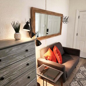 Una habitación con un aparador de madera, un espejo, una lámpara, un sofá con cojines y una alfombra estampada.