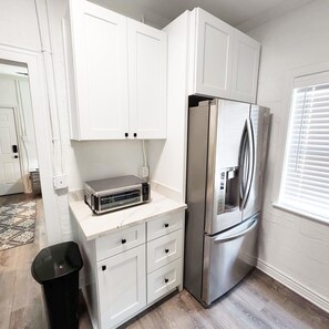 Una cocina compacta con armarios blancos, un refrigerador de acero inoxidable y un horno tostador integrado.