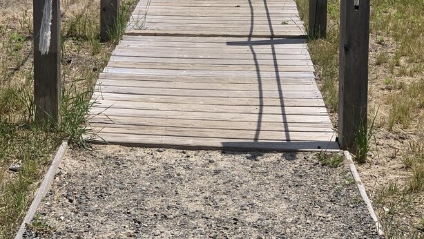 Una passerella di legno che conduce a una spiaggia, con un cartello che dice 'Welcome'.