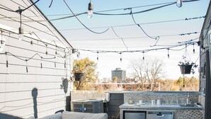 Eine Terrasse im Freien mit einer integrierten Küche, einem weißen Sofa und einem Feuerkorb.