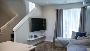 Ein modernes Wohnzimmer mit Flachbildfernseher, einer Couch, einem Couchtisch und einer Treppe.