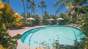 A swimming pool surrounded by palm trees and lounge chairs.