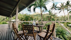 A wooden deck with a round table and chairs, overlooking a lush tropical landscape with palm trees and greenery.