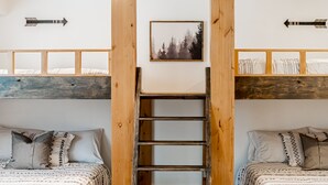 A room with two beds, a ladder, and a framed picture on the wall.